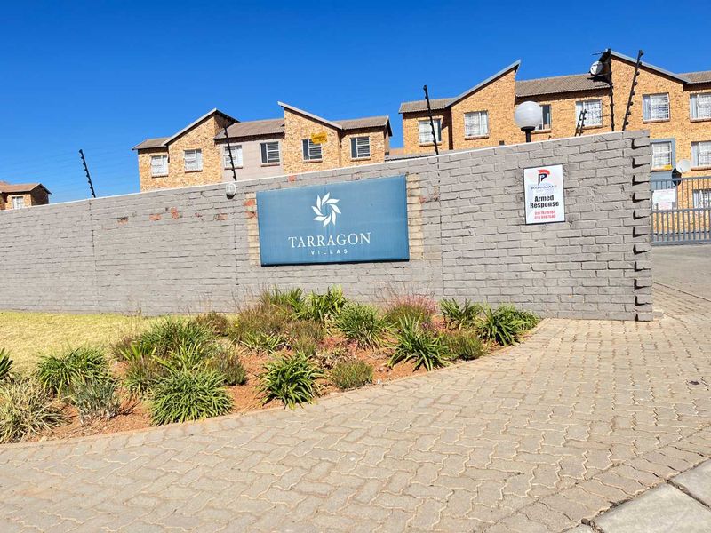Front entrance view of Tarragon Villas featuring a brick boundary wall, electric fencing, and paved driveway access.