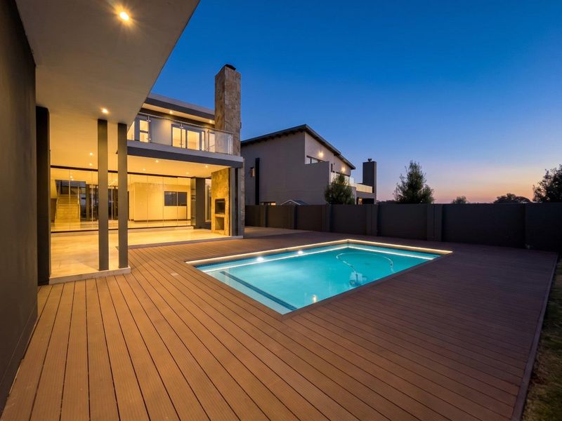 Modern outdoor entertainment area featuring a swimming pool, timber decking, and a built-in fireplace, set against a contemporary home facade at dusk.
