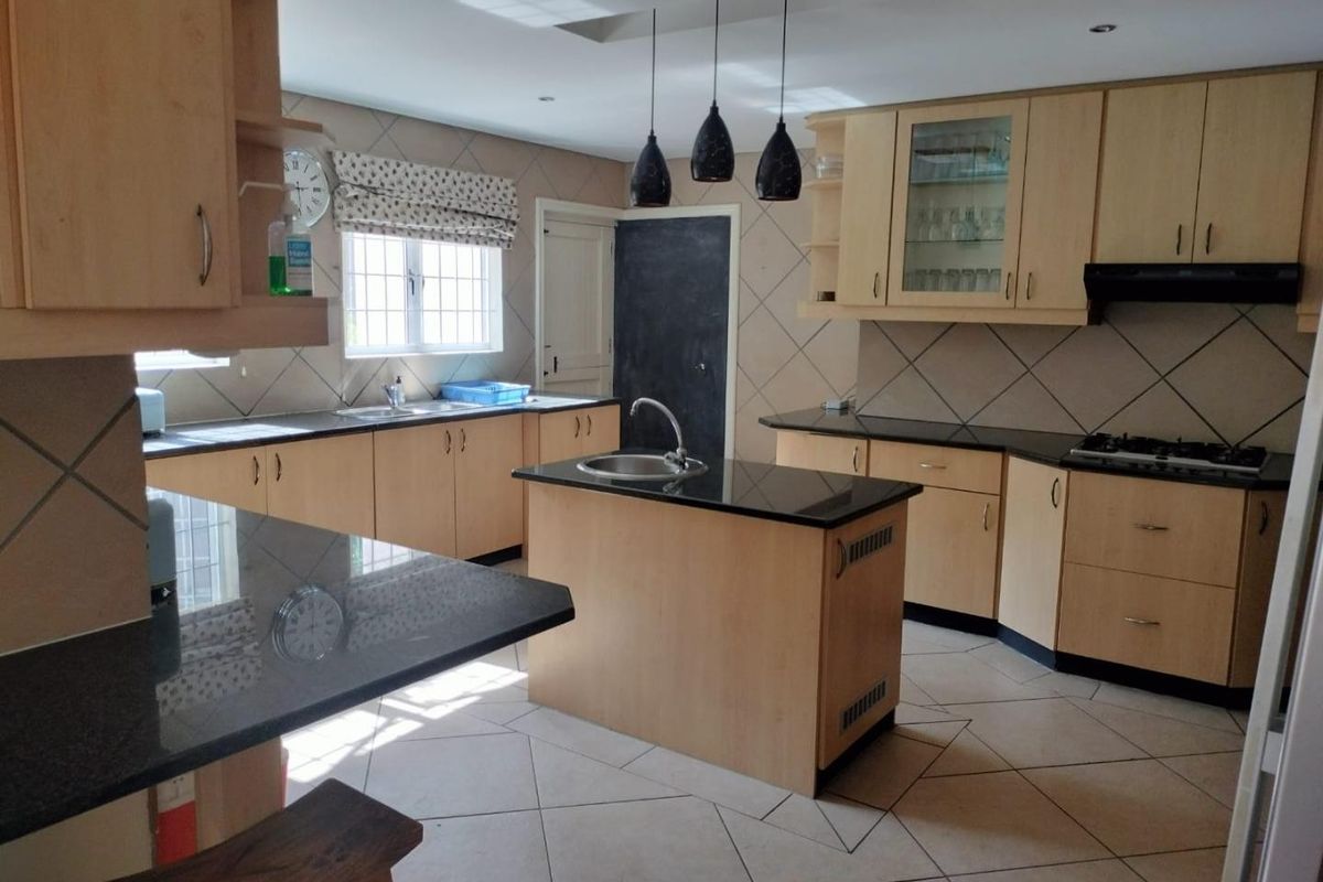 Spacious kitchen featuring light wood cabinetry, dark granite countertops, a central island with sink, gas hob, and tiled flooring.
