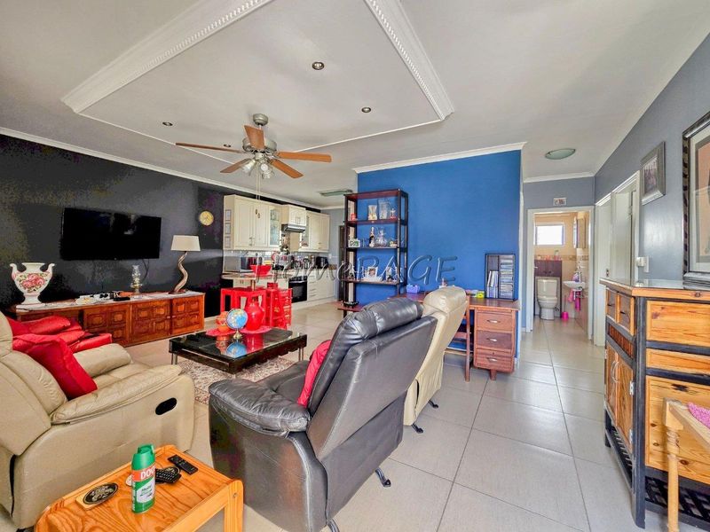 Open-plan living area featuring tiled floors, crown molding, and a functional kitchen with built-in cabinetry, seamlessly connecting to the main living space.