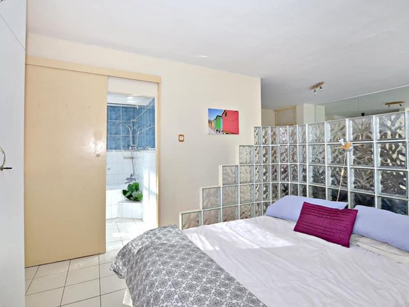 Bedroom featuring a glass block partition, mirrored wall, built-in wardrobe, and direct access to an en-suite bathroom with tiled finishes.