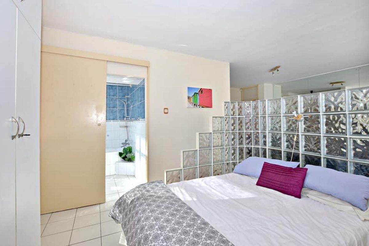 Bedroom featuring a glass block partition, mirrored wall, built-in wardrobe, and direct access to an en-suite bathroom with tiled finishes.