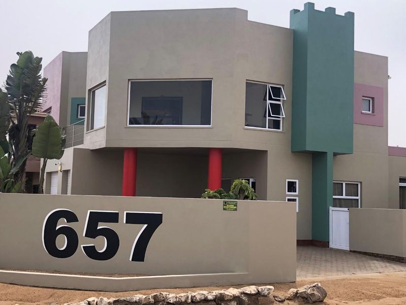 Front elevation of a multi-level residential property featuring a prominent boundary wall, paved driveway, and distinctive architectural facade with decorative columns.