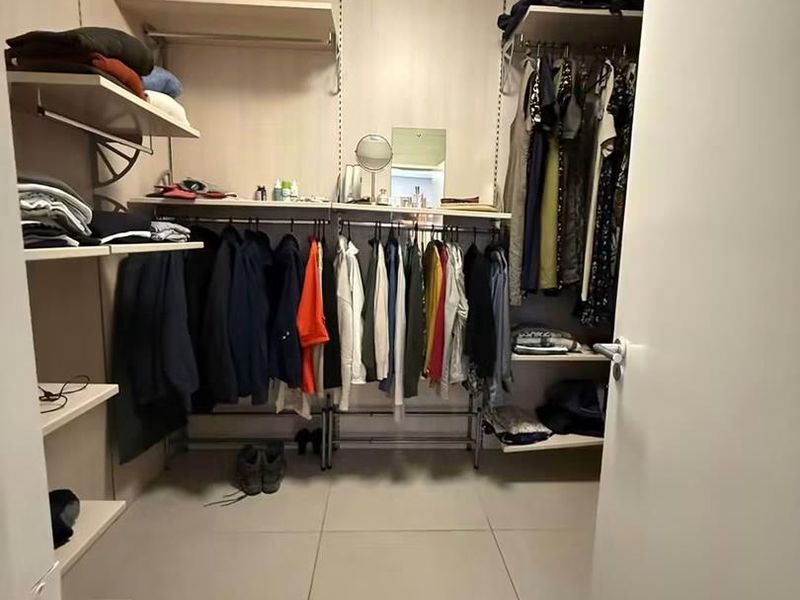 A functional walk-in closet featuring organized built-in shelving, hanging rails, and neutral tiled flooring.