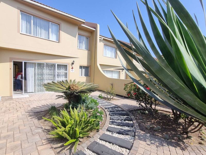 A well-maintained rear exterior view of the townhouse featuring a paved patio area, landscaped garden, and sliding glass doors with security gates.