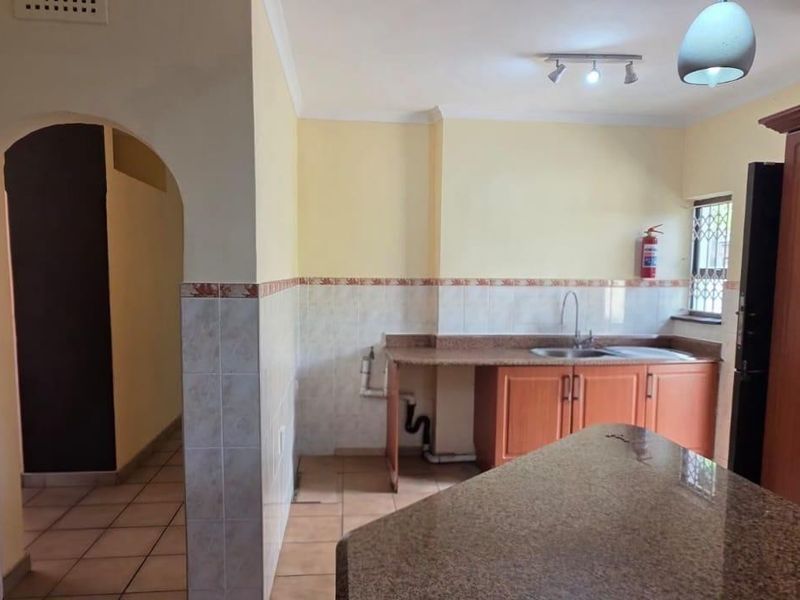 Kitchen featuring granite countertops, wooden cabinetry, and tiled finishes, with an open archway leading to adjacent living areas.