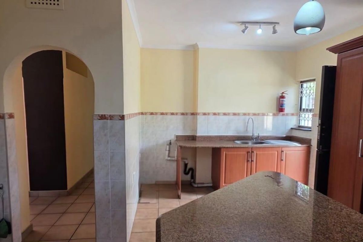 Kitchen featuring granite countertops, wooden cabinetry, and tiled finishes, with an open archway leading to adjacent living areas.