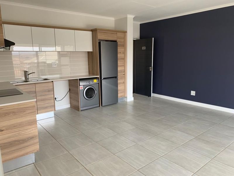 Modern open-plan kitchen and living area featuring contemporary wood-finish cabinetry, tiled flooring, and a sleek, neutral design suitable for various interior styles.