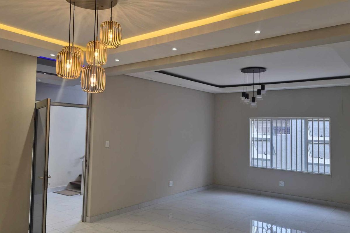 Spacious living area featuring modern recessed and cove lighting, neutral tiled floors, and a built-in shelving unit, offering a clean and contemporary aesthetic.
