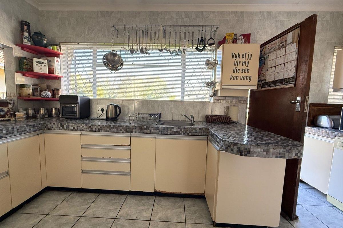 A dated kitchen featuring tiled countertops, light-colored cabinetry, and a window above the sink area.