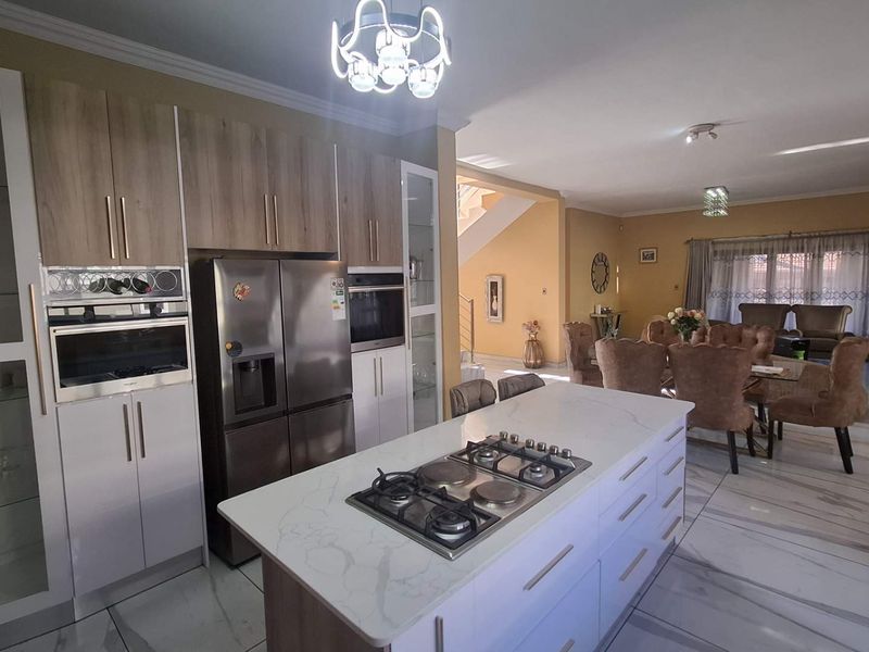 Spacious open-plan kitchen and dining area featuring a central island with gas hob, modern cabinetry, and elegant marble-look floor tiles throughout.