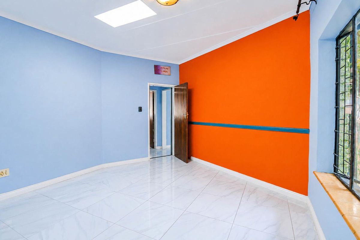 A bright, empty bedroom featuring tiled flooring, a skylight, and bold accent walls, providing a versatile space ready for personalization.