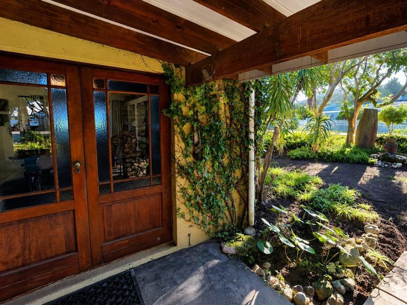 A charming entrance featuring timber double doors, exposed wooden beams, and a landscaped garden area with a concrete porch.
