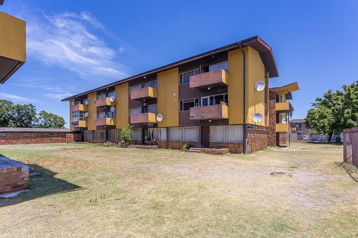 Rear view of a multi-story apartment building featuring private balconies and a shared open lawn area.