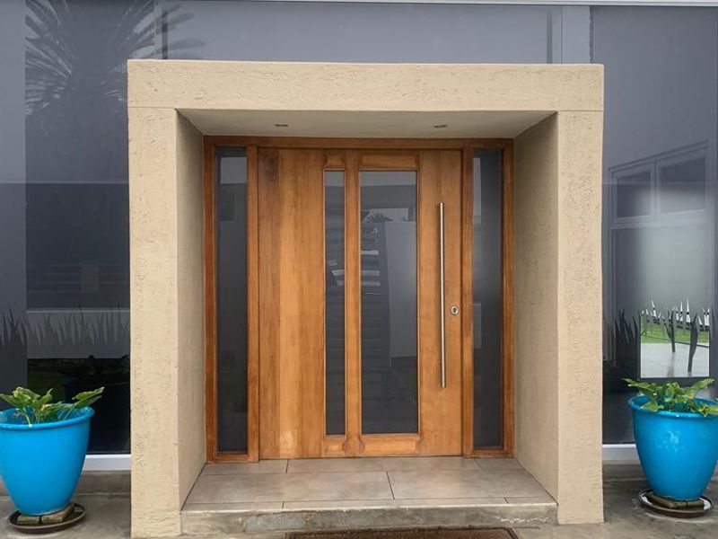 Modern front entrance featuring a substantial timber pivot door with glass sidelights, set within a clean, contemporary recessed porch structure.