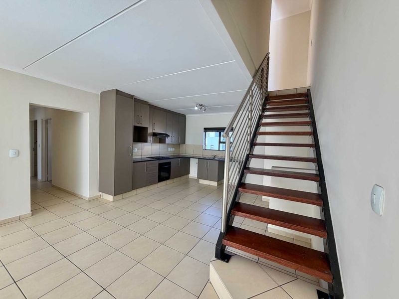 Open-plan living area featuring a modern kitchen with built-in cabinetry and appliances, tiled flooring, and a staircase with a metal balustrade.