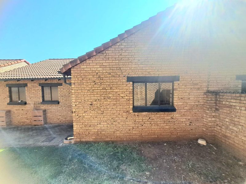 Rear view of the townhouse featuring face brick exterior, tiled roofing, and paved patio area with black metal window frames.