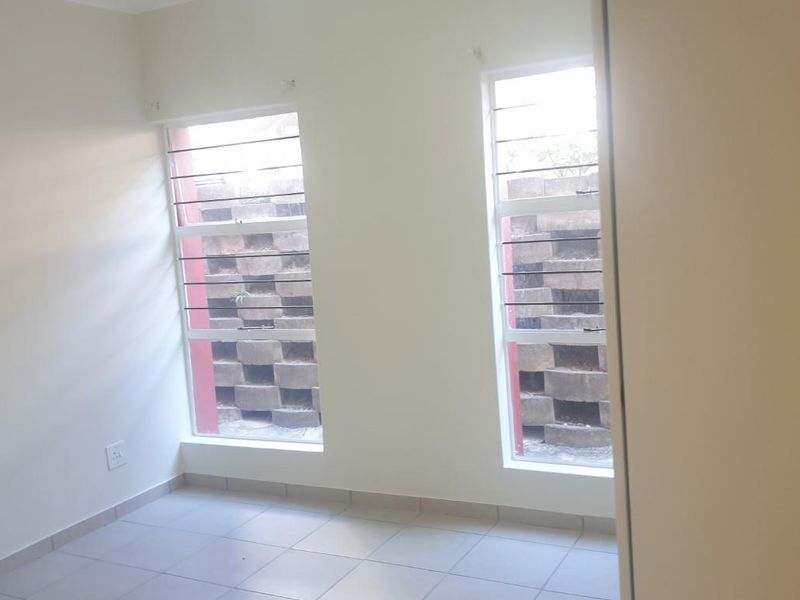 A bright, empty bedroom featuring tiled flooring and dual vertical windows with security bars, offering a clean and neutral space ready for personalization.