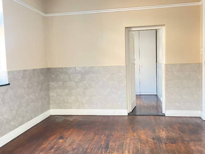 An empty bedroom featuring original hardwood flooring, wainscoting, and a doorway leading to a built-in cupboard area.