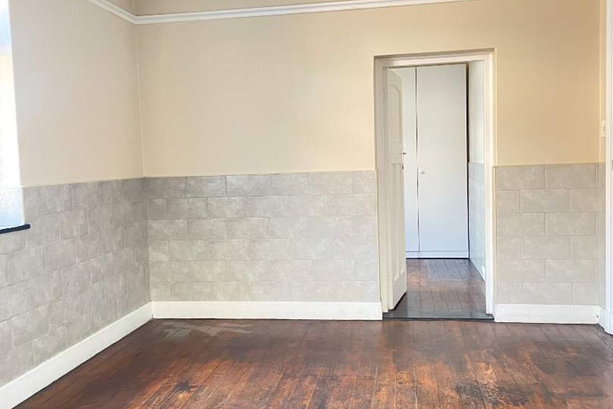 An empty bedroom featuring original hardwood flooring, wainscoting, and a doorway leading to a built-in cupboard area.