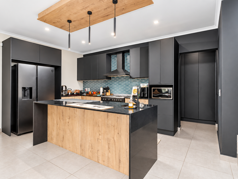 Modern kitchen featuring dark cabinetry, a wood-accented island with stone countertops, a tiled backsplash, and integrated appliances.