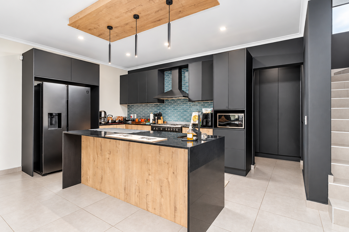 Modern kitchen featuring dark cabinetry, a wood-accented island with stone countertops, a tiled backsplash, and integrated appliances.