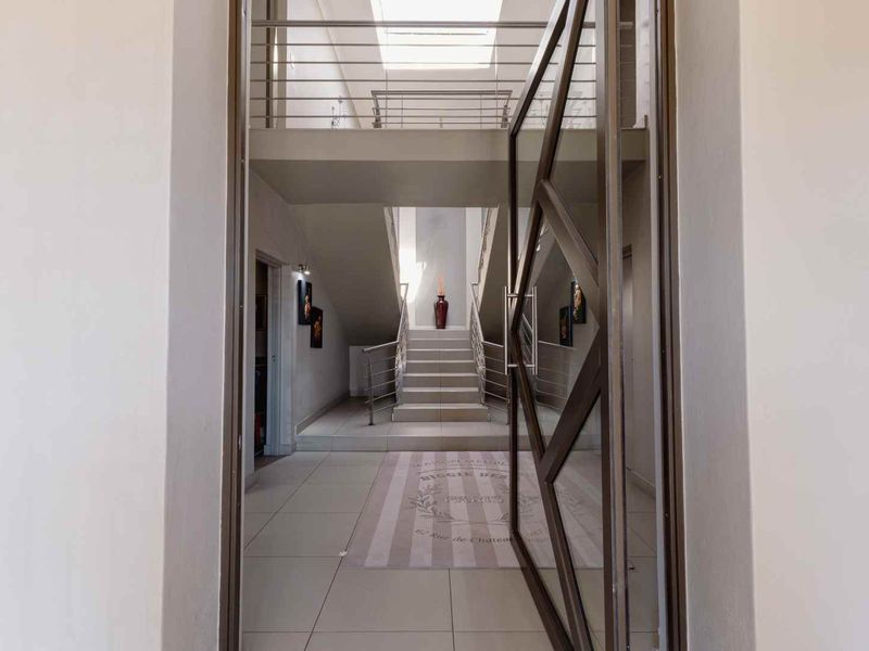 Spacious entrance hall featuring a modern staircase with metal balustrades, large pivot door, and a skylight providing ample natural light.