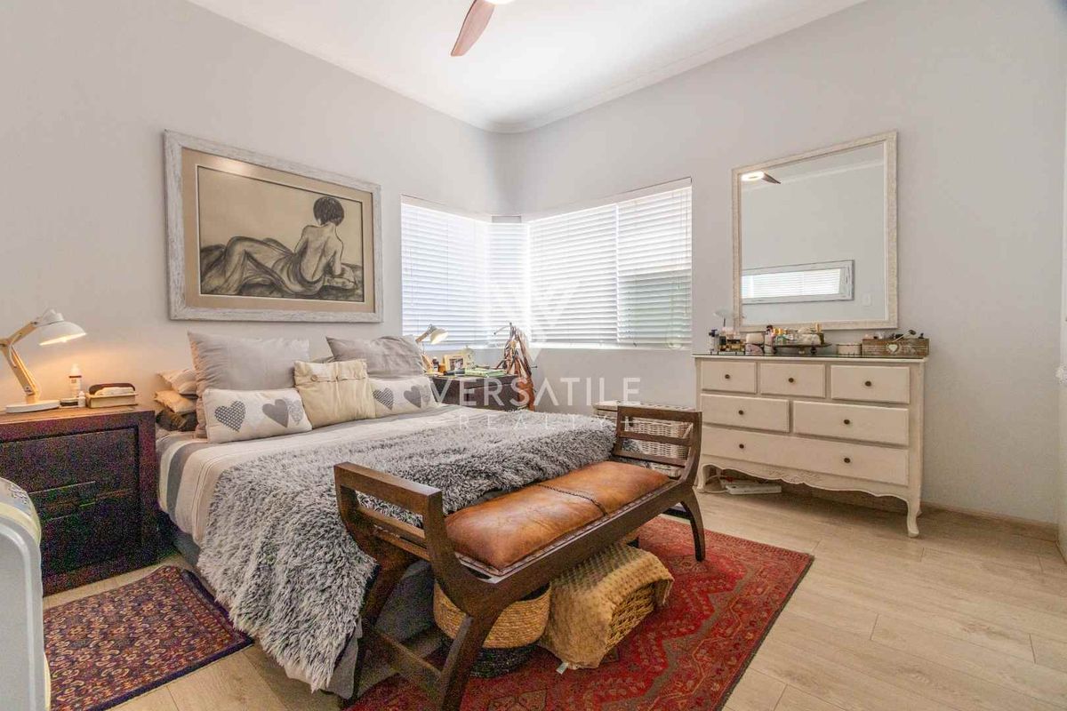 A well-maintained bedroom featuring light-toned laminate flooring, a ceiling fan, and a bay window with fitted venetian blinds.