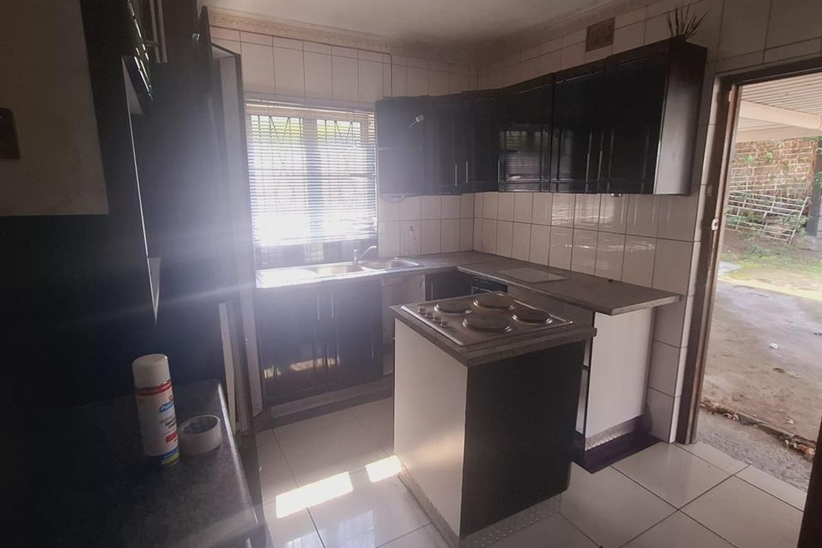 A functional kitchen featuring dark built-in cabinetry, a central island with an electric hob, tiled flooring, and direct access to the exterior.