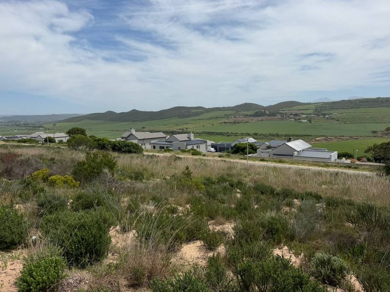 A scenic view overlooking a residential estate with rolling green hills and mountains in the background.