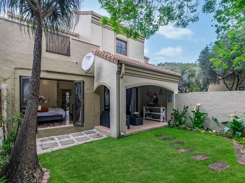 Rear view of the townhouse featuring a covered patio, well-maintained garden, and direct access to the interior through sliding doors.