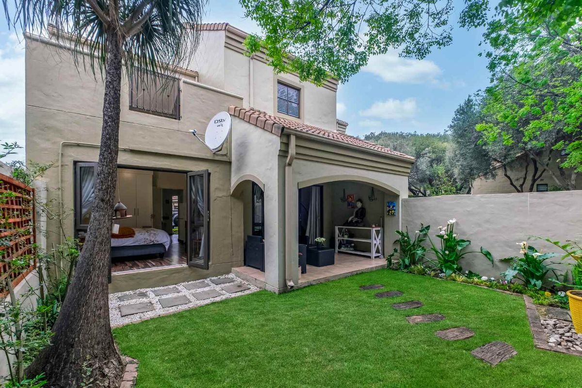 Rear view of the townhouse featuring a covered patio, well-maintained garden, and direct access to the interior through sliding doors.
