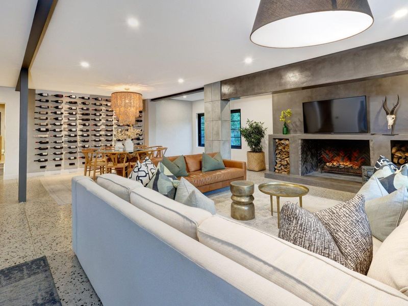 Spacious open-plan living area featuring a striking concrete fireplace, integrated wine storage wall, and polished terrazzo flooring with modern recessed lighting.