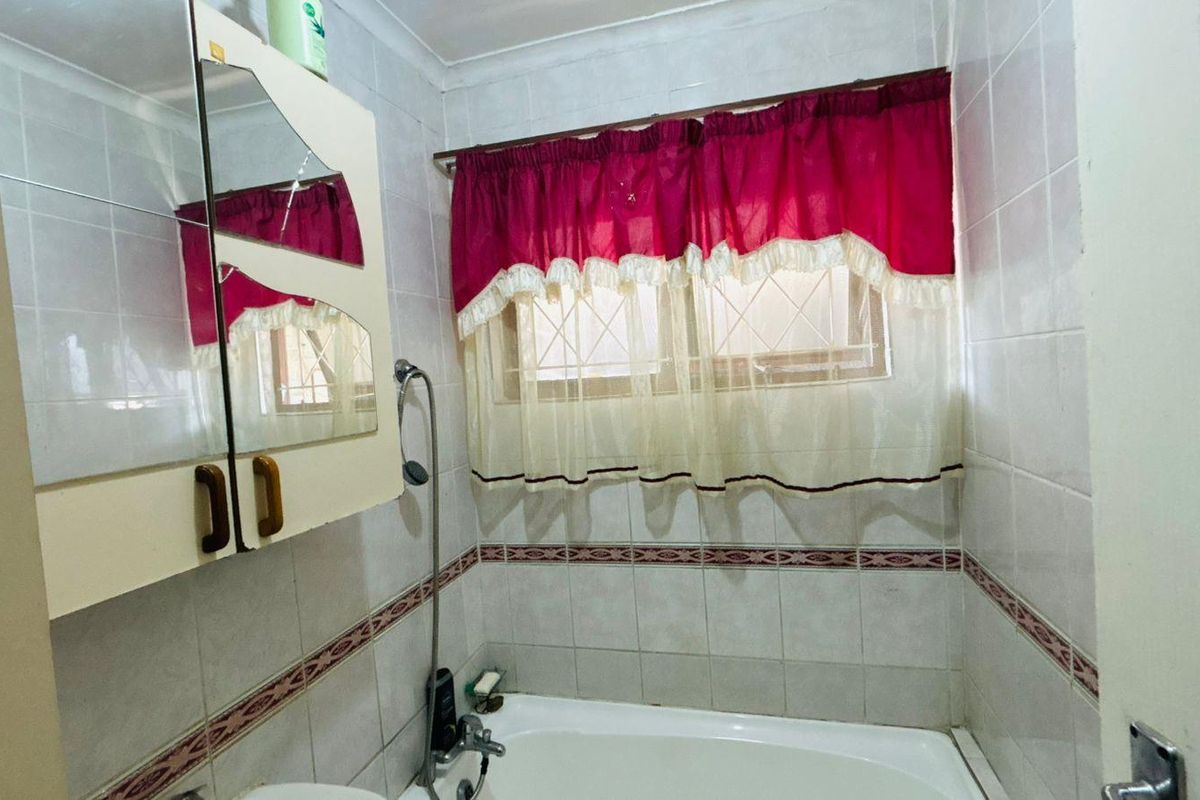 A functional bathroom featuring a bathtub with shower attachment, wall-mounted vanity cabinet, and tiled walls.