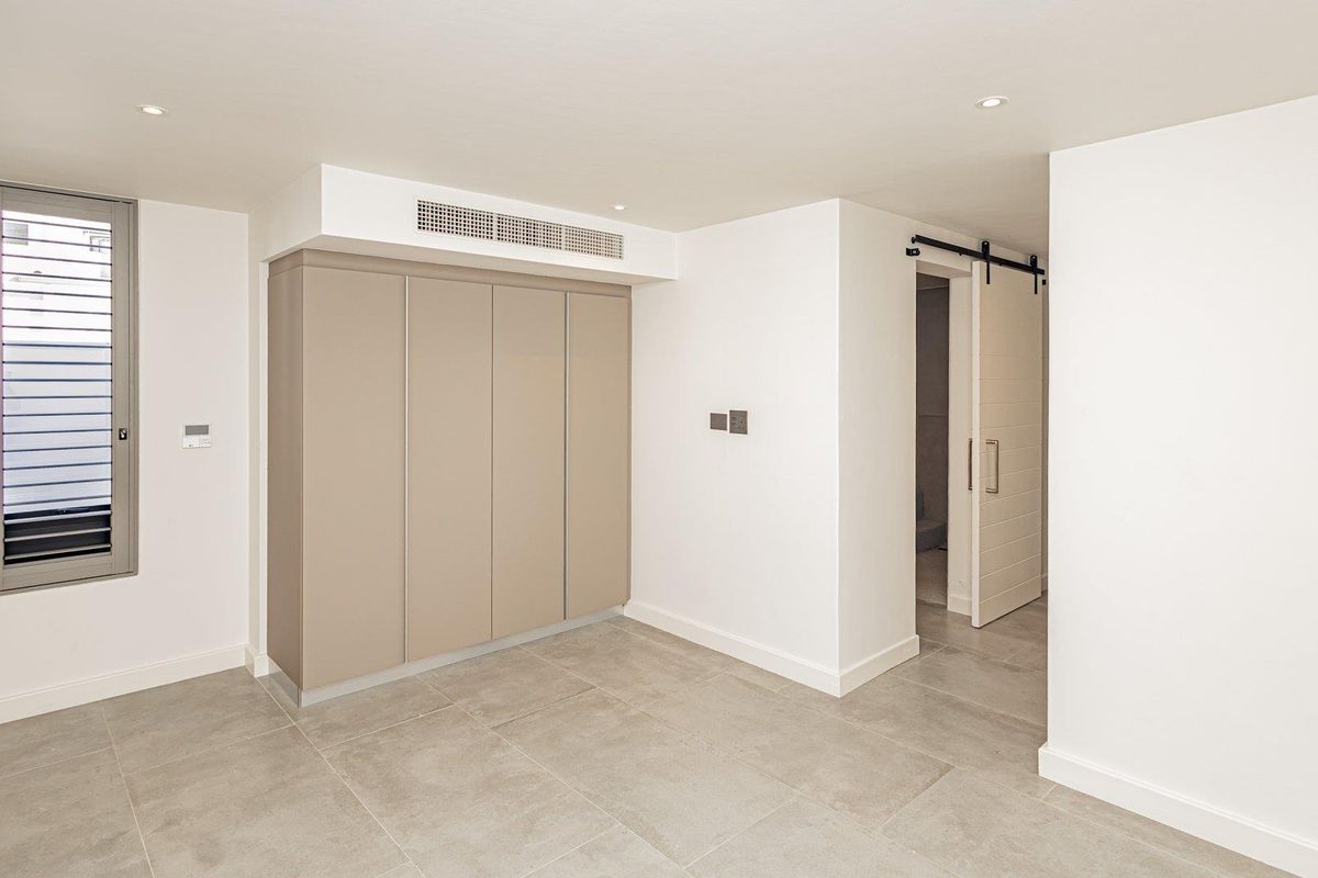 A modern, minimalist bedroom featuring neutral tiled flooring, built-in cabinetry, a sliding barn door, and integrated ducted air conditioning.