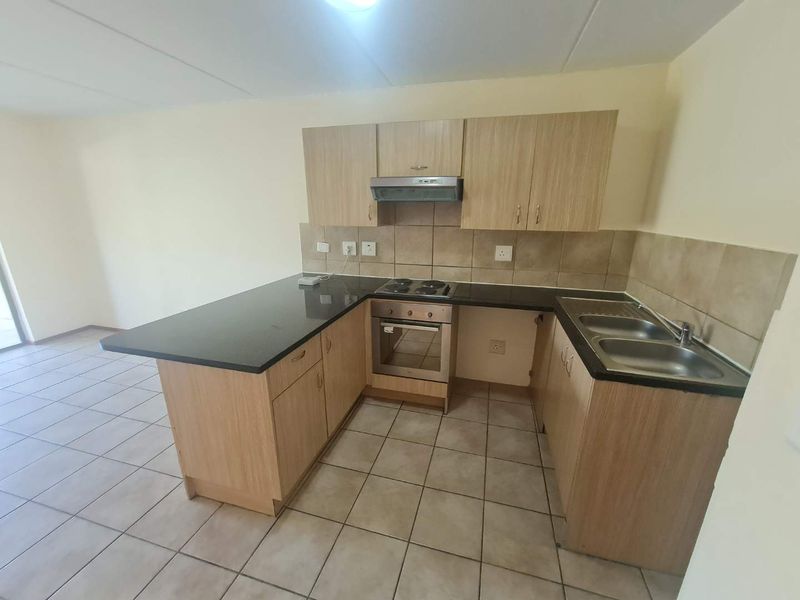 A functional kitchen featuring light wood-finish cabinetry, dark granite countertops, built-in oven, electric hob, and a double stainless steel sink with tiled flooring.