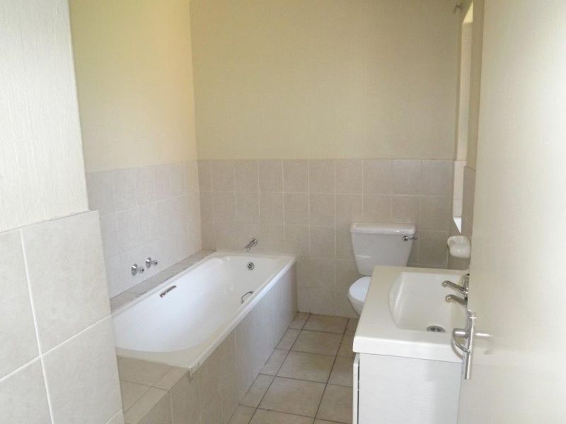 A functional bathroom featuring a built-in bathtub, a standard toilet, and a vanity basin with neutral wall and floor tiling.