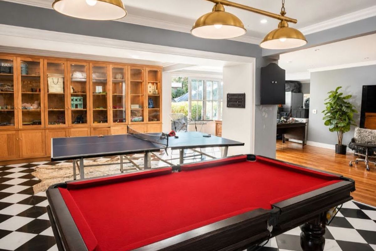 Spacious living area featuring built-in wooden cabinetry, crown molding, and a mix of hardwood and checkered tile flooring, illuminated by pendant lighting.