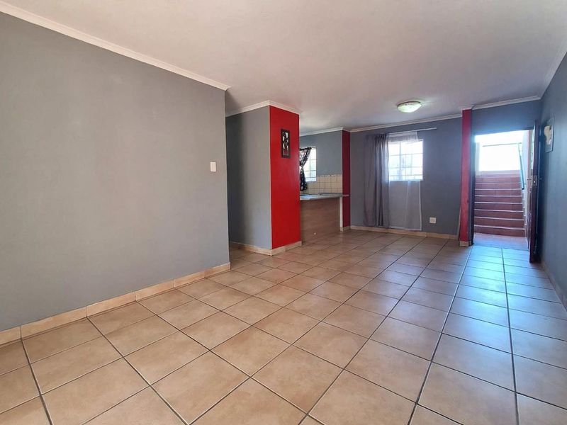 An open-plan living and kitchen area featuring neutral tiled flooring, grey and red accent walls, and direct access to an external staircase.