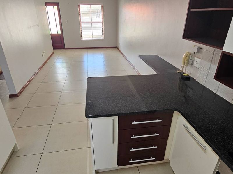 An open-plan living and kitchen area featuring tiled flooring, granite countertops, and built-in cabinetry, offering a clean and functional layout.