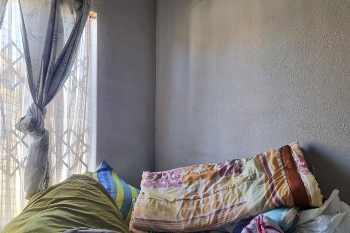 A bedroom featuring a window with a security gate, showing signs of wear on the walls and ceiling requiring maintenance and cosmetic updates.