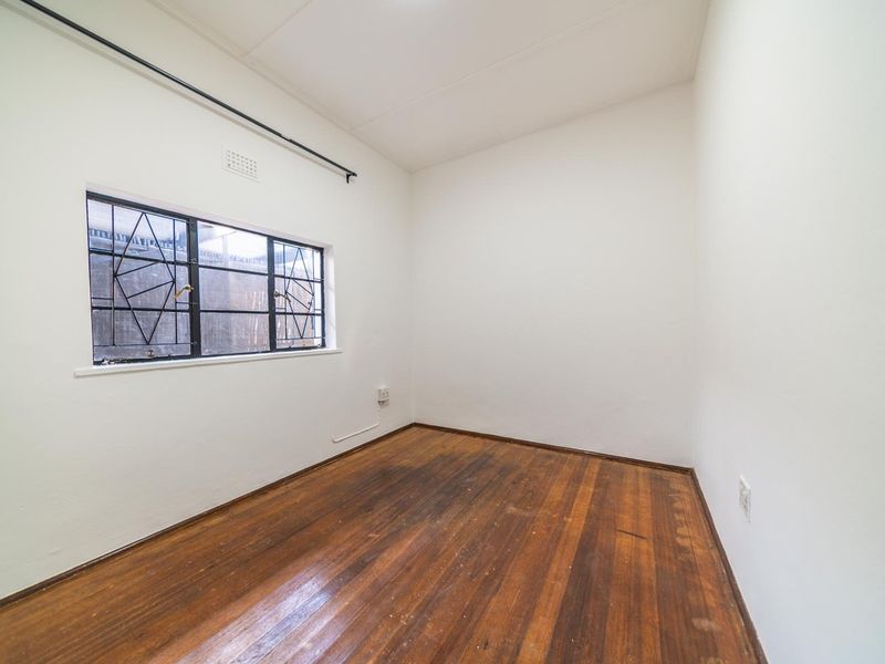 An empty bedroom featuring original timber flooring, white walls, and a window fitted with security bars.