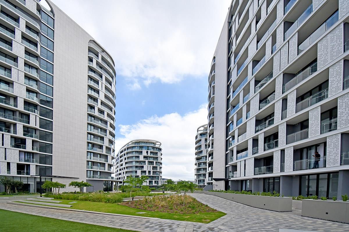 Modern apartment complex featuring contemporary architectural design, glass balconies, and landscaped communal garden areas between the residential buildings.