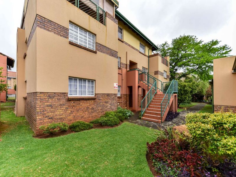 Rear view of the townhouse complex featuring a brick and plaster facade, external staircase with metal railings, and a well-maintained communal garden area.