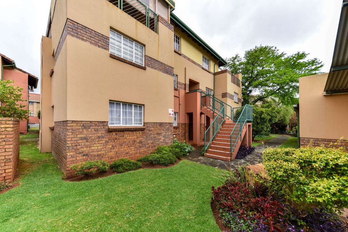 Rear view of the townhouse complex featuring a brick and plaster facade, external staircase with metal railings, and a well-maintained communal garden area.