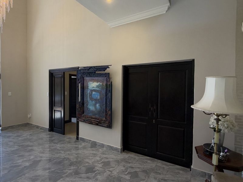 Spacious grand entrance hall featuring high ceilings, a crystal chandelier, and polished marble-look flooring with elegant double-door access.