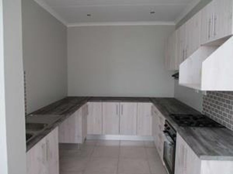 A clean, modern kitchen featuring light wood-finish cabinetry, dark laminate countertops, a built-in oven with gas hob, and a stylish tiled backsplash.