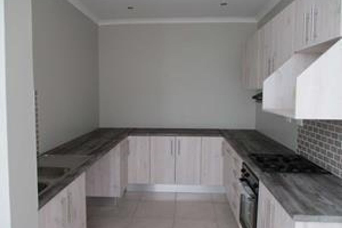 A clean, modern kitchen featuring light wood-finish cabinetry, dark laminate countertops, a built-in oven with gas hob, and a stylish tiled backsplash.