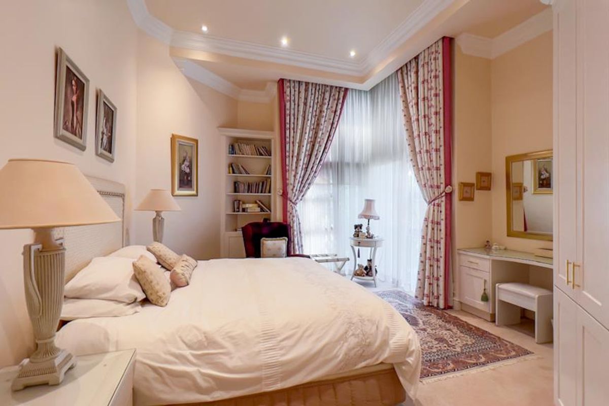 A well-maintained bedroom featuring built-in cabinetry, recessed ceiling lighting, crown molding, and large windows with floor-to-ceiling curtains.