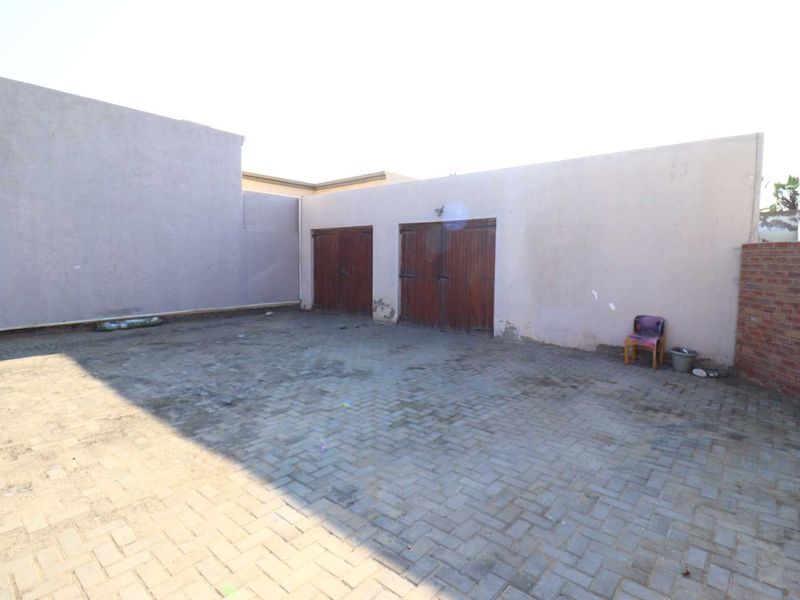 A paved outdoor area featuring a double garage with wooden doors and surrounding brick boundary walls.